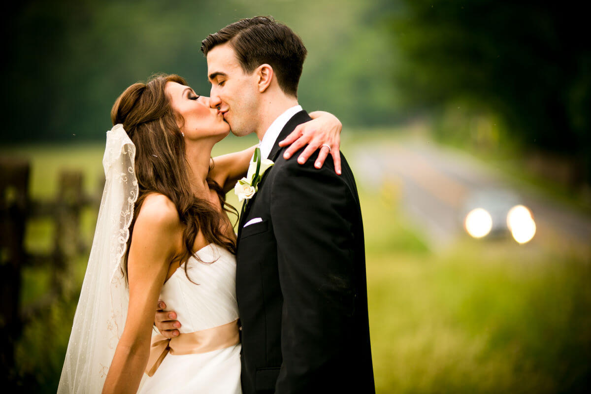 Bride And Groom Kissing In The Countryside Filled With Green Nature