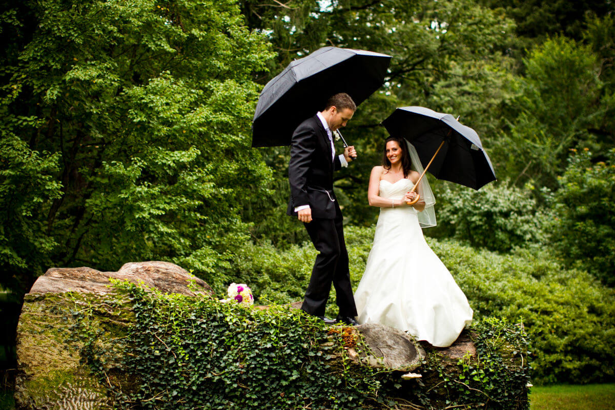 Elegant Wedding Couple Taking A Stroll Through The Garden With Umbrellas