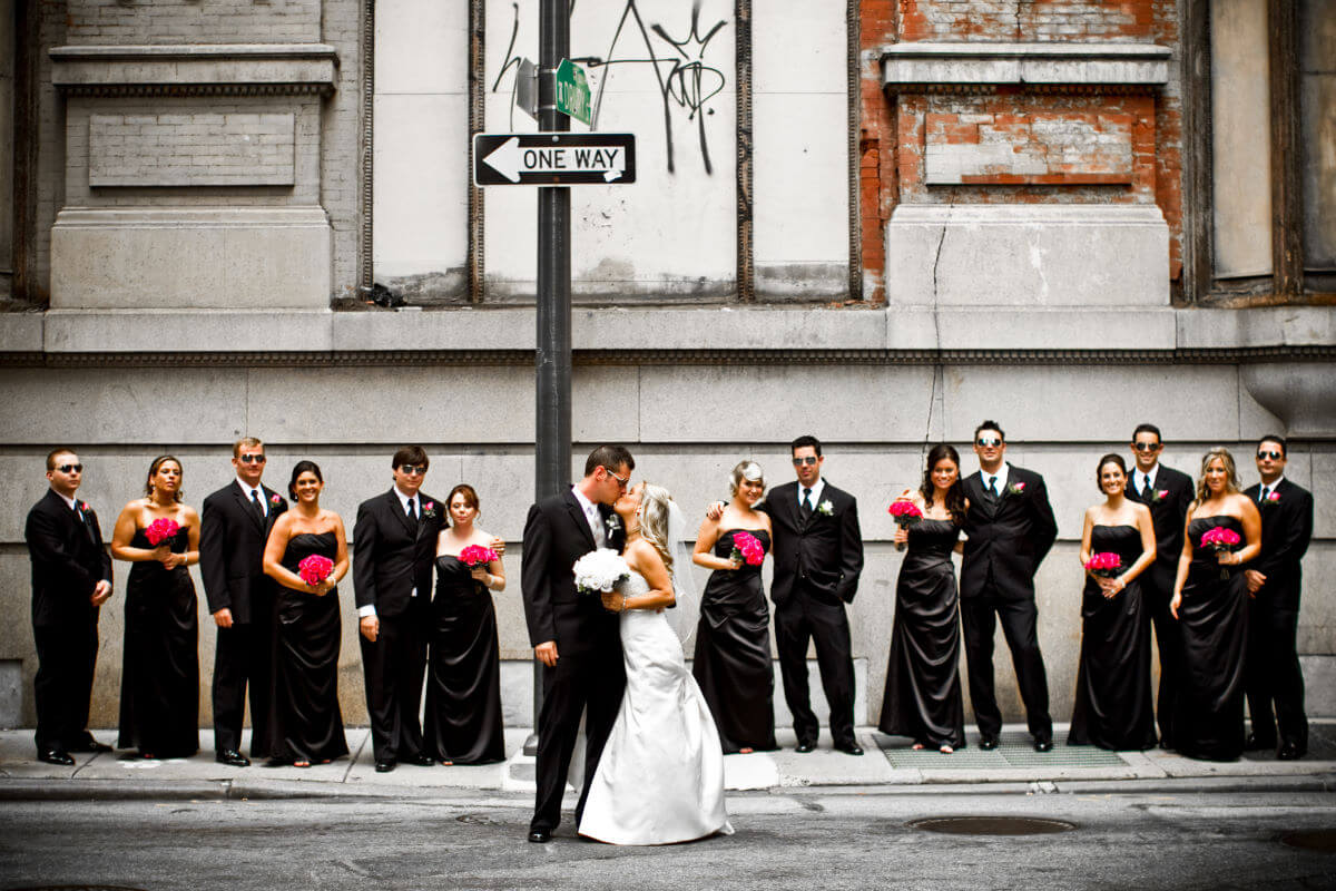 Kissing Bride And Groom Pose For A Fun Portrait With Their Friends